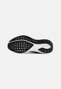 Semelle de chaussure avec un dessous en caoutchouc noir texturé comportant des motifs circulaires et rectangulaires, une semelle intercalaire blanche et des bords lisses.