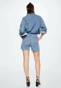 Ensemble en jean comprenant une chemise et un short de couleur bleu clair. La chemise possède un col classique et des manches retroussées ; le short a une taille haute et des poches au dos.