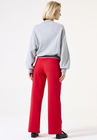 Sweat-shirt oversized gris avec épaules tombantes, associé à un pantalon rouge taille haute. Modèle portant des chaussures noires, vue de dos.