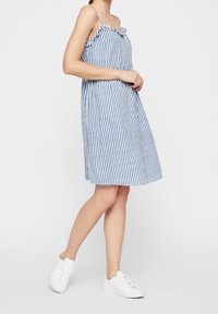 Robe d'été rayée bleu et blanc avec détail à volants au niveau du col, corsage ajusté et jupe ample. Associée à des baskets blanches.