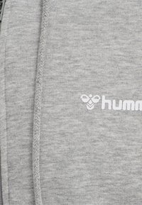 Grå sweatshirt med en mjuk textur, med dragkedja och broderad logotyp i vitt. Tyget visar en lätt melerad mönstring.