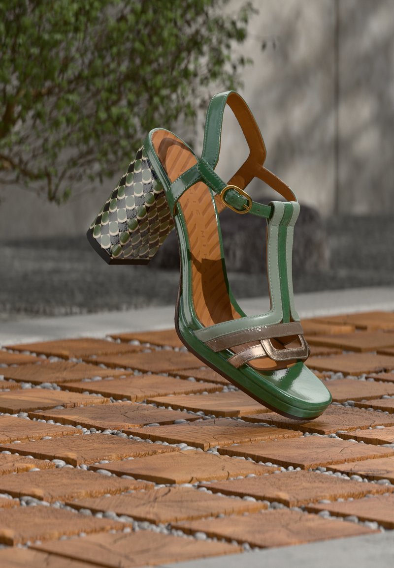 Πράσινο σανδάλι από πατενταρισμένο δέρμα με δομημένο σχήμα, μεταλλικές λεπτομέρειες και τακούνι τύπου block με σχέδιο. Διαθέτει λουράκια και κούμπωμα με αγκράφα.