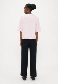 Light pink short-sleeve top with a loose fit, paired with black ribbed wide-leg pants and chunky black shoes.