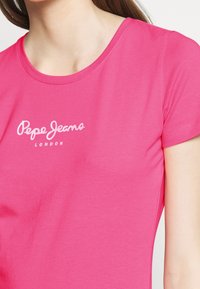Bright pink T-shirt with short sleeves and a round neckline. Features white "Pepe Jeans London" logo printed on the front. Soft material texture.
