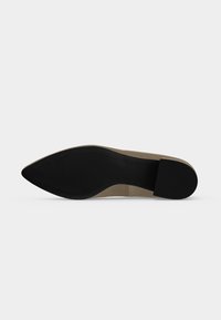 Semelle d'une chaussure à bout pointu avec semelle noire et talon bloque, empeigne beige visible sur le côté sur fond blanc uni.