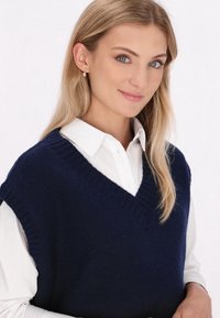 Marineblaues Strickwesten mit V-Ausschnitt, über einem weißen Hemd mit Kragen getragen, zeigt gerippte Kanten und eine weiche Textur.