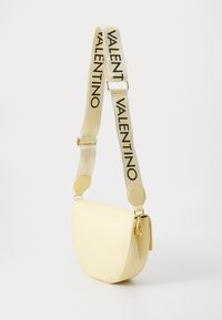 Borsa a spalla gialla in pelle con forma curvata, marchio impresso e tracolla in tessuto con testo nero "VALENTINO". Accenti hardware eleganti.