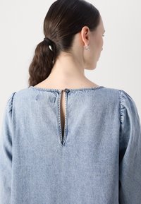 Helles blauer Denim-Oberteil mit Puffärmeln, einem runden Ausschnitt und einem Knopfverschluss im Rücken mit einem Schlüssellochdetail. Glatte Textur.