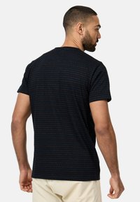 Schwarzes T-Shirt mit kurzen Ärmeln, das ein dezentes Streifenmuster mit bunten Akzenten aufweist. Der Stoff wirkt weich und hat eine lockere Passform.