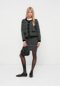 Veste en tweed noir et blanc avec un col contrastant, assortie d'une jupe coordonnée. Portée avec des ballerines noires et un sac à main texturé noir.