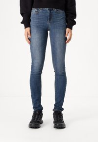 Smala blå denimjeans med hög midja, femficksdesign och subtila slitningar. Bärs med svarta utomhusskor.