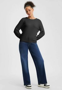 Czarny, teksturowany sweter z wzorem w plaster miodu, okrągły dekolt i długie rękawy, w połączeniu z niebieskimi spodniami o szerokich nogawkach i czarnymi sneakersami.