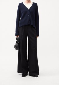 Tmavě modrý pletený cardigan s výstřihem do V, se třemi knoflíky, doplněný o černé široké kalhoty s vysokým pasem a malou černou kabelku.
