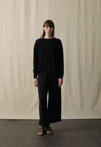 Top negro de manga larga con cuello redondo y pantalones de pierna ancha. Tejido suave con un ajuste relajado, combinado con sandalias oscuras. Diseño sencillo, con detalles mínimos.