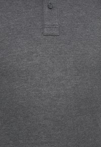 Polo shirt gris foncé en tissu texturé, avec un col, une patte de boutonnage à deux boutons et des détails de couture près de l'ourlet.