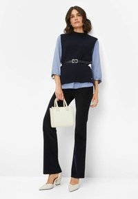 Marineblauer, gerippter, ärmelloser Pullover mit einem schwarzen Gürtel, über einer hellblauen Bluse getragen, kombiniert mit schwarzen Hosen und weißen High Heels.