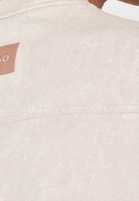 Gros plan du haut du dos d'une personne portant une chemise texturée beige clair avec un petit patch en cuir rectangulaire partiellement visible.