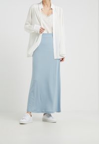 Ljusblå maxikjol gjord av mjukt tyg, matchad med en vit skjorta med knappar och vita sneakers. Kjolen har en enkel, flödande design.