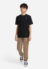 Sort T-shirt med korte ærmer og et lille logo, sat sammen med khaki elastiske bukser og sorte sneakers med hvide såler.