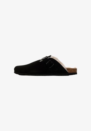 Zoccolo in suede nero con foderatura in pelliccia sintetica bianca, suola in sughero e fibbia regolabile nera, caratterizzato da una punta rotonda e suola in gomma testurizzata.