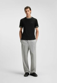 Sort kortærmet t-shirt med grøn kant, parret med lysegrå, løstsiddende bukser. Sorte sko fuldender outfittet.