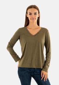 Camicia a maniche lunghe verde oliva con scollatura a V e tre bottoni decorativi sul colletto. Tessuto morbido, vestibilità comoda, abbinata a jeans scuri.