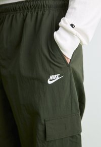 Olivenfarvede cargobukser med elastisk talje, der har et hvidt Nike-logo og sidelommer. Fremstillet af letvægtsstof med en glat overflade.