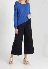 Maglietta blu a maniche lunghe, vestibilità ampia, abbinata a pantaloni in denim neri a gamba larga. Accentuata con sneaker multicolori e un design casual e testurizzato.