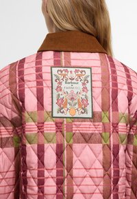 Καπιτονέ μπουφάν σε ροζ, μπορντώ και πράσινη καρό διάταξη με κοτλέ γιακά. Διαθέτει διακοσμητική ετικέτα με ανθισμένο σχέδιο στην πλάτη.