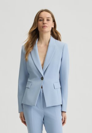 Lichtblauwe blazer van gladde stof, met een enkele knoopsluiting, gesneden revers en twee voorzakken. Getailleerde pasvorm.