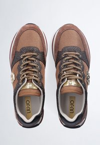 Sneaker in rete e suede marrone con intricati motivi scuri e lacci dorati. Presenta un accento metallico vicino alla caviglia e una soletta ammortizzata.