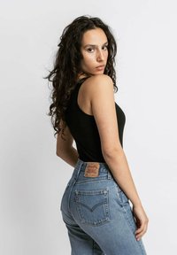 Top a manica lunga nera aderente abbinato a jeans a vita alta blu chiaro. Dettagli notevoli includono una toppa in pelle sulla vita posteriore e cuciture classiche.