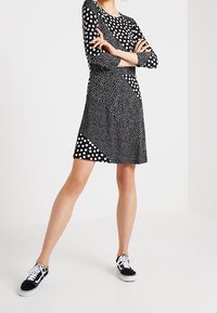 Robe noire à pois blancs, manches trois quarts, et jupe à motifs diagonaux. Associée à des baskets noir et blanc.