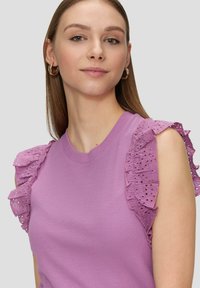 Paarse mouwloze top met een geribbelde textuur en decoratieve kanten ruffles op de schouders. Minimalistische ronde halslijn.