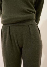 Zielono-oliwkowy sweter z dzianiny z pasującymi spodniami, z rypsowym pasem w talii i bocznymi kieszeniami, wykonany z miękkiego, teksturowanego materiału.