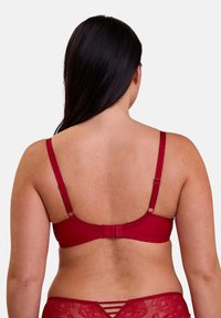 Soutien-gorge rouge avec bretelles réglables, détails en dentelle texturée et fermeture à crochets au dos. Tissu lisse avec une coupe ajustée.