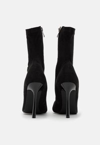 Bottines à talons en suède noir au design épuré, avec un haut talon aiguille et une fermeture éclair sur le côté pour un enfilage facile.