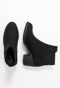 Czarne botki za kostkę wykonane z miękkiego zamszu, z teksturowaną gumową podeszwą, falbaniastym wykończeniem oraz średniej wysokości słupkowym obcasem.