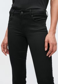 Jeans neri realizzati in tessuto elasticizzato con design aderente. Presentano una chiusura con bottone, passanti per cintura e tasche anteriori. Tessuto liscio.