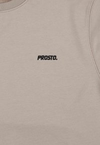 Beżowa bluza z teksturowanej tkaniny, z prążkowanym okrągłym dekoltem i małym czarnym haftowanym logo "PROSTO." z przodu.