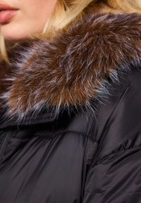 Czarna kurtka puchowa z grubym, brązowym kołnierzem z sztucznego futra z szarymi końcówkami, gładka w dotyku, z zapięciem na zamek, zaprojektowana z myślą o ciepłości.