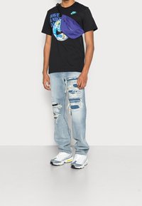 Svart t-shirt med blå grafik och slogan, slitna ljusblå jeans, lila midjeväska och grå sneakers med gula detaljer.