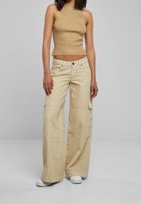 Beżowe spodnie cargo o szerokich nogawkach, z przednimi kieszeniami i guzikiem na pasku. Do tego dopasowany prążkowany beżowy top i białe trampki.