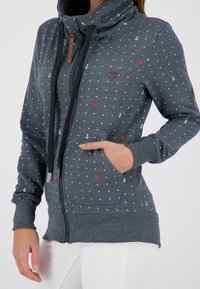Felpa grigia con zip, colletto alto, motivo a pois, dettagli rossi e design di ancore. Dispone di tasche e polsini a coste.