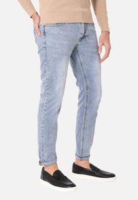 Jeans in denim blu chiaro con una vestibilità slim, caratterizzati da un leggero sbiadimento e orli arrotolati. Abbinati a sneaker nere slip-on.