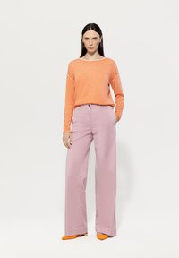 Bright orange long-sleeve sweater, light pink wide-leg pants, and orange pointed shoes. Smooth textures and relaxed fit.
