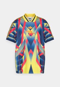 Dres Adidas s geometrickým designem v žluté, modré a červené barvě. Obsahuje vyšívané logo a kontrastní pruhované rukávy.