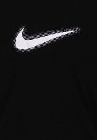 Camiseta de tela negra con un logo de Nike en patrón de puntos en color blanco. El logo está ubicado en la parte superior izquierda.