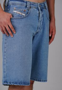 Light blue denim shorts with a loose fit, featuring a visible pocket label, copper rivets, and stitched hems. Smooth texture.