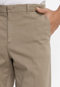 Pantaloni beige con design a vita piatta, texture liscia e tasche laterali. Realizzati in tessuto leggero, con una vestibilità dritta classica.